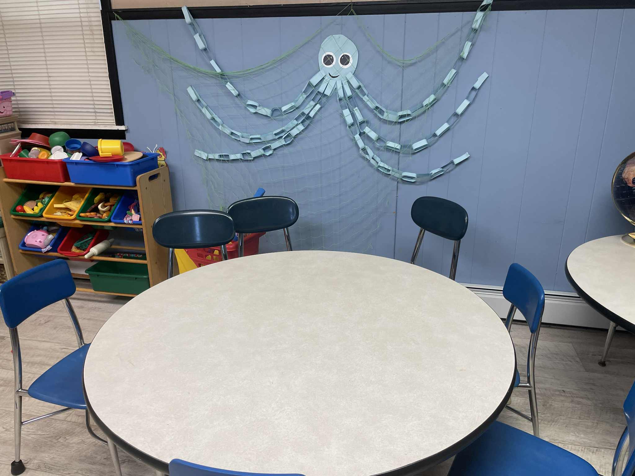 Bright classroom with round tables, blue chairs, and cheerful octopus wall decoration